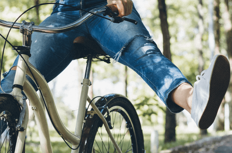 A person on a bike in the woods with her feet off the pedals.